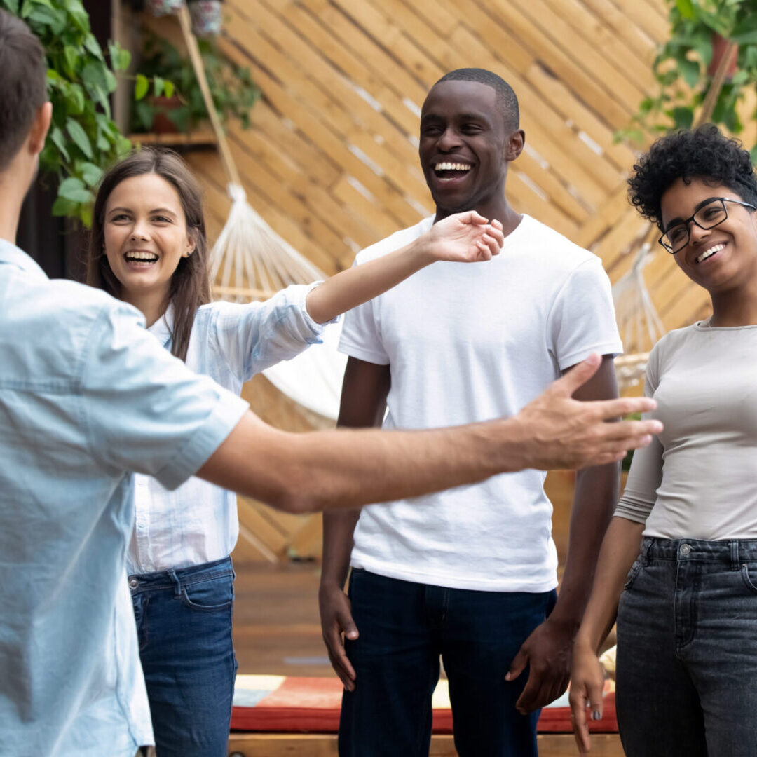 Overjoyed smiling multiracial millennial friends hug embrace meeting young man colleague in caf , excited happy diverse young people laugh hang out together greeting pal at casual gathering